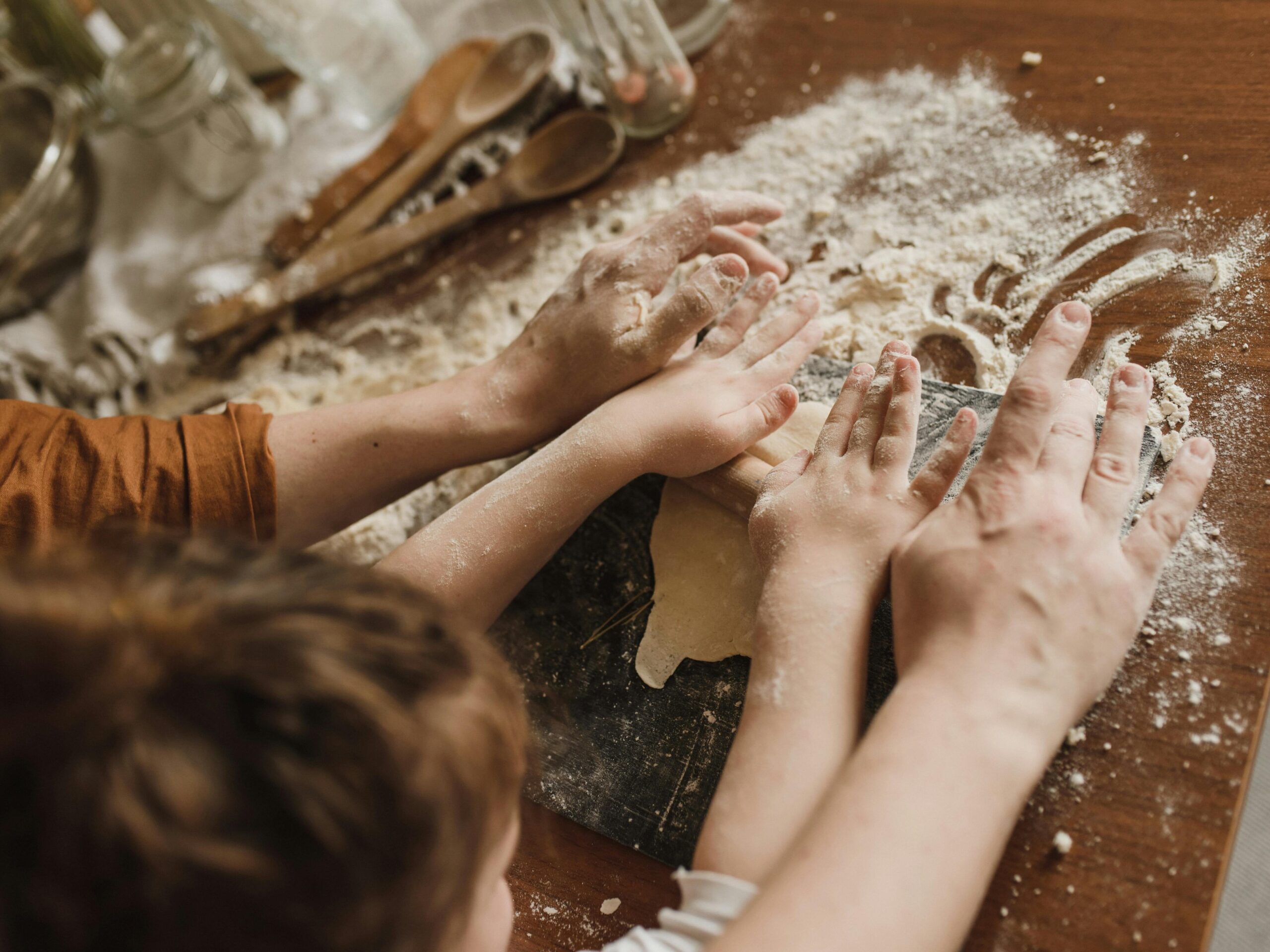 A parent and child bonding while kneading dough in a messy kitchen environment.